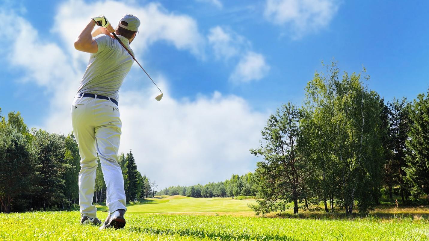 A man dressed in beige and white swings his club at a golf course in a section about the renowned PGA courses in Dorado Beach. 