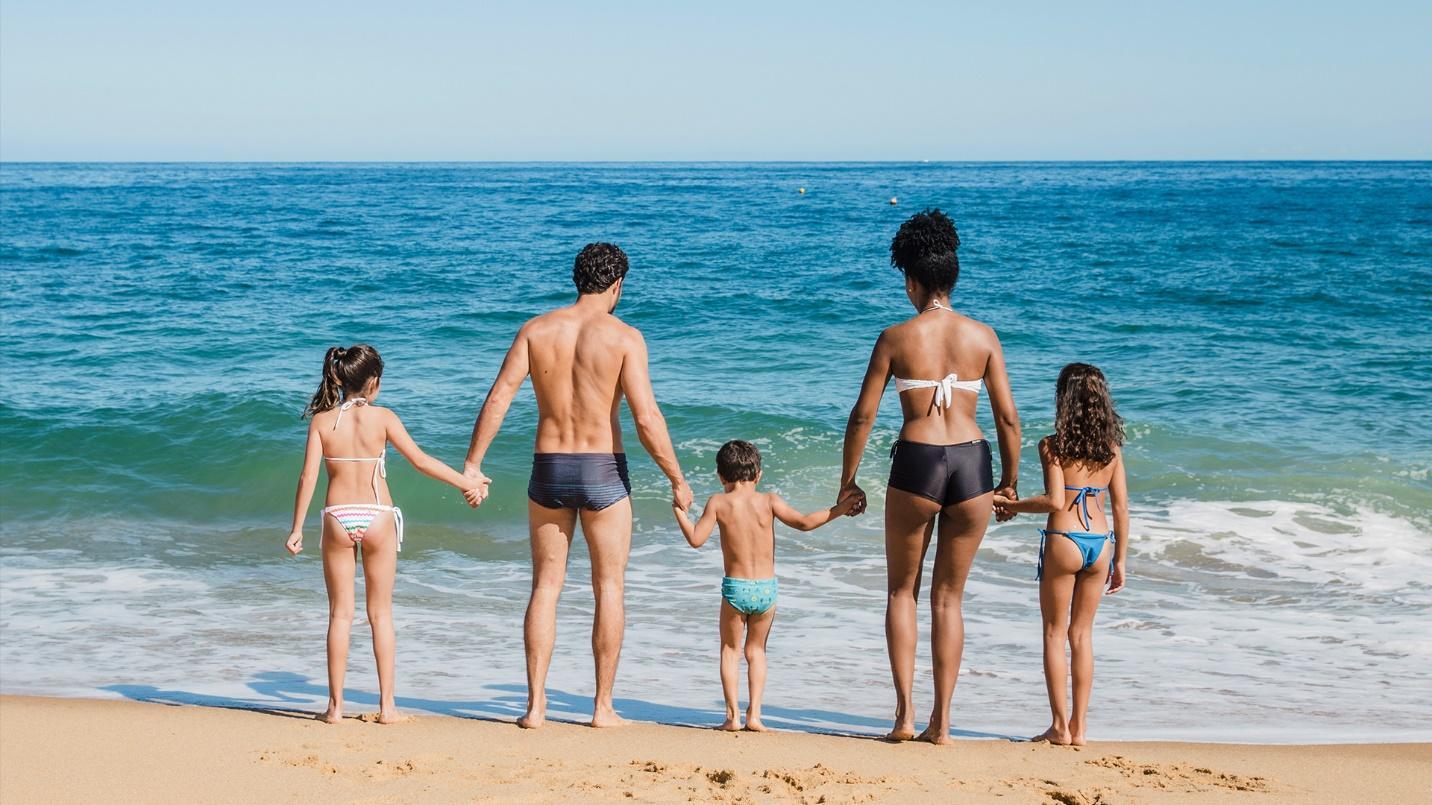 Family members in swimsuits hold hands while standing at the shoreline in a section about peaceful and family-friendly Dorado Beach. 