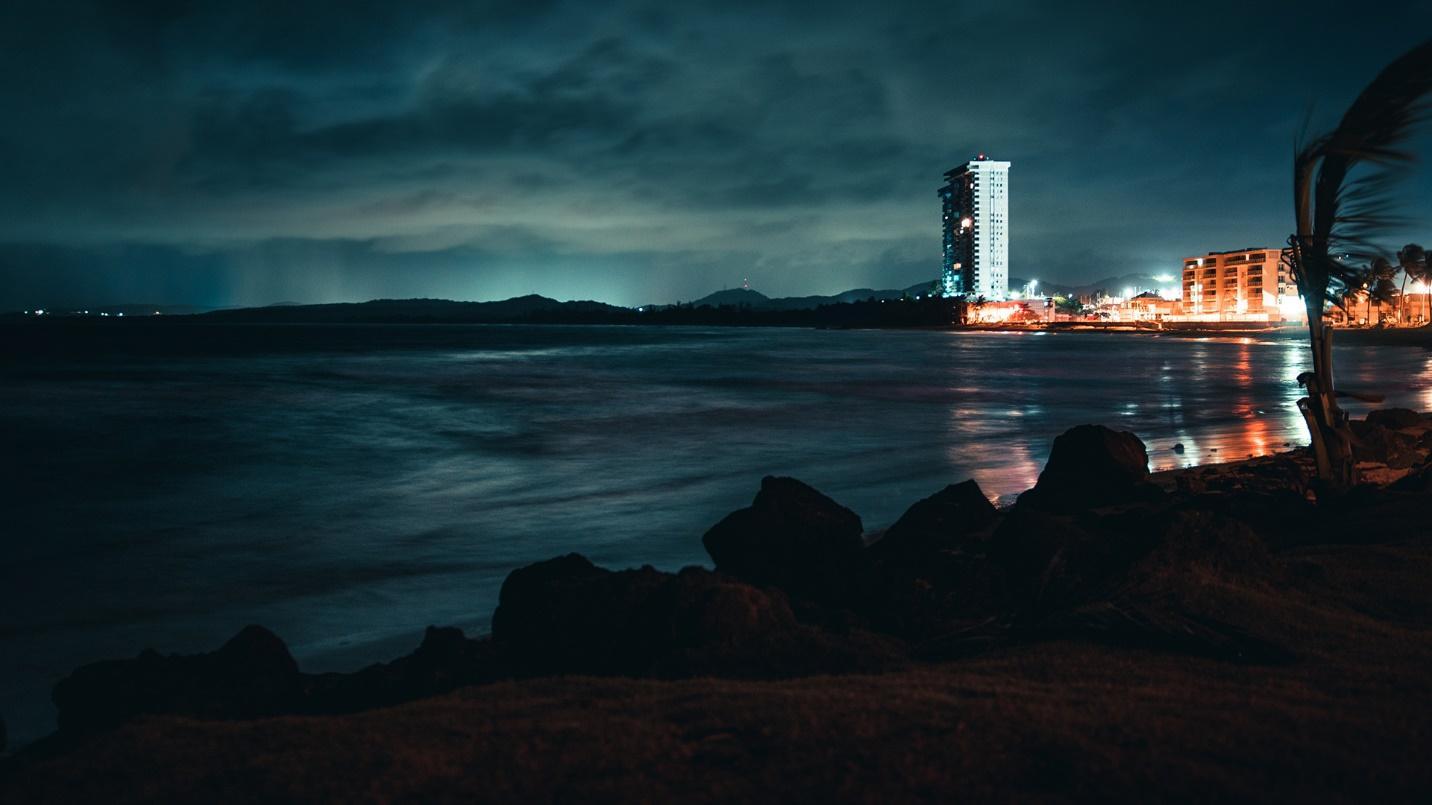 Dark waters framed by a night-time sky, shoreline, and buildings in a section about Luquillo Beach. 