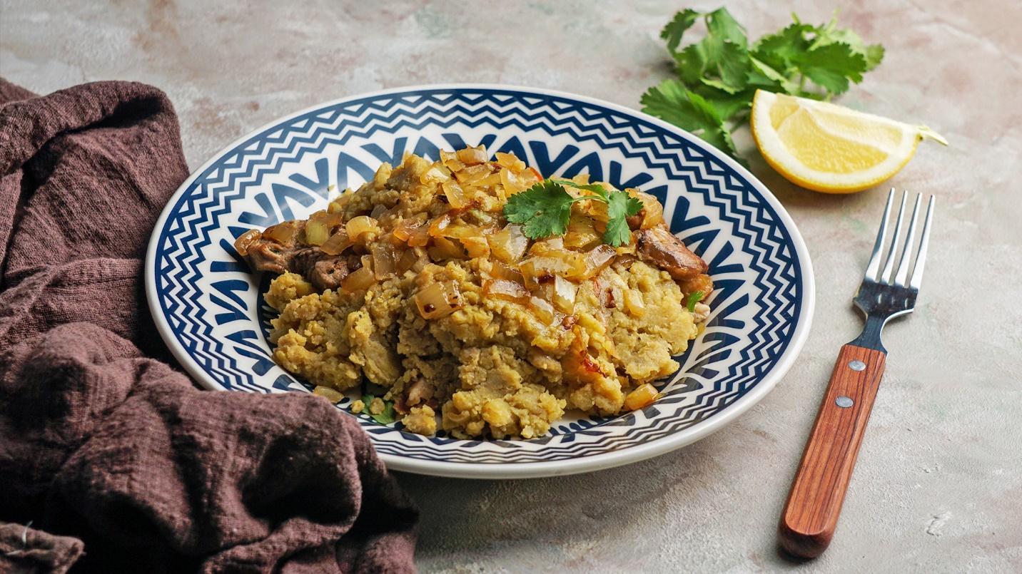 A plate of mofongo beside a towel, lemon slice, parsley, and fork in a section about Puerto Rican cuisine. 