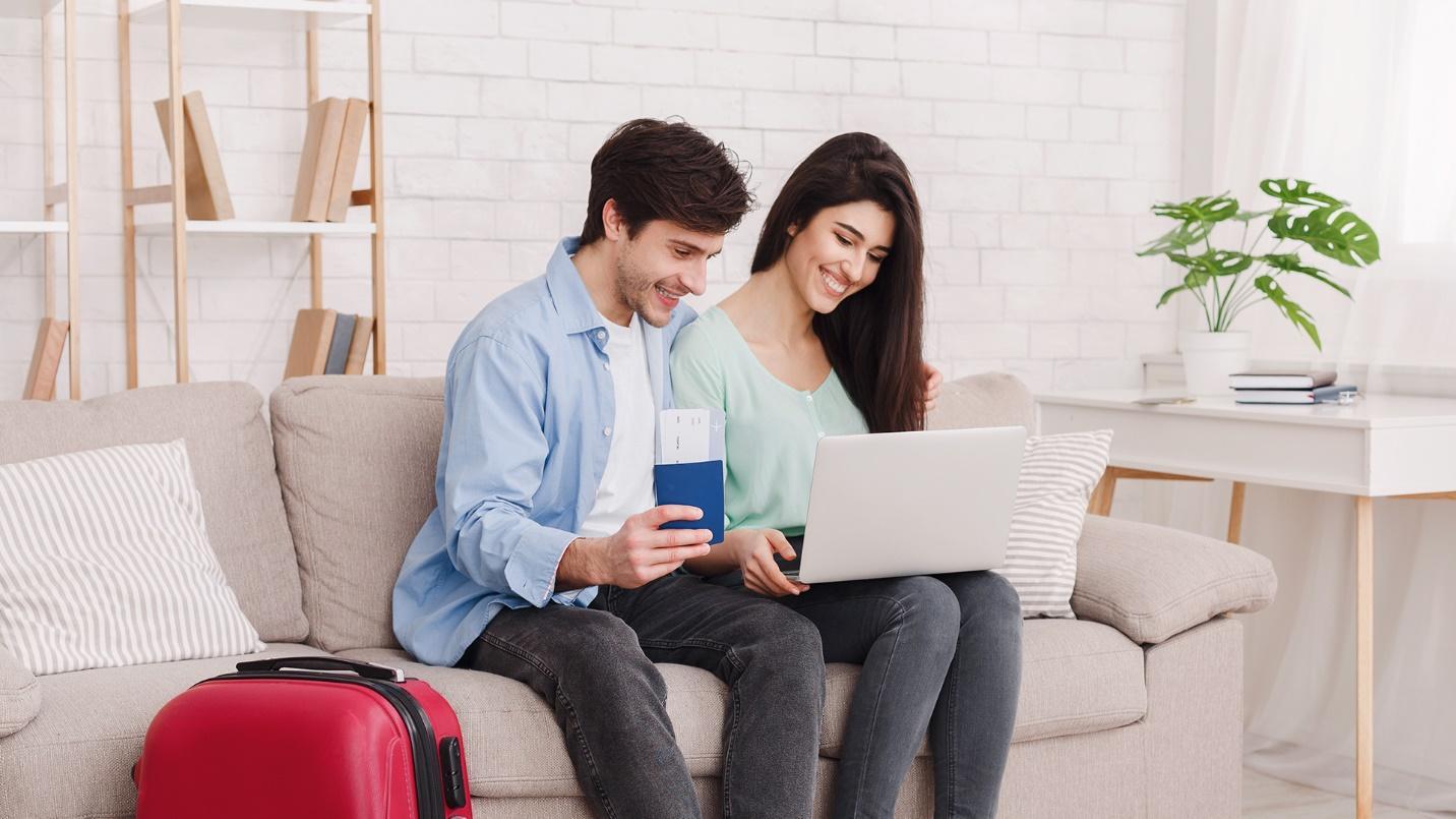 A young smiling couple sit on a couch and look at a laptop screen in a section about how to plan a vacation in Puerto Rico. 