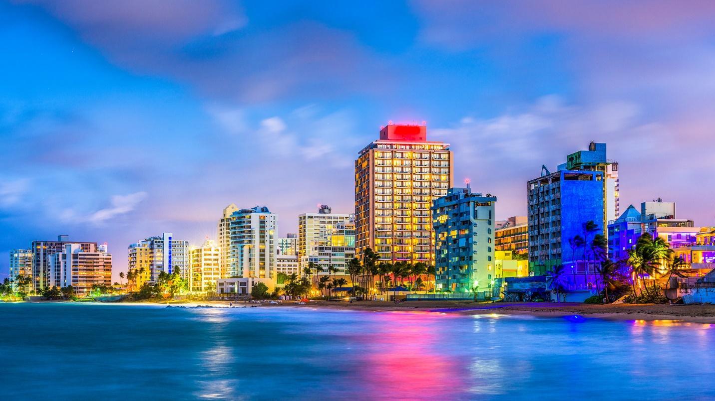 Beachfront properties and palm trees framed by blue sea and sky in a section previewing a guide to the neighborhood of Condado.