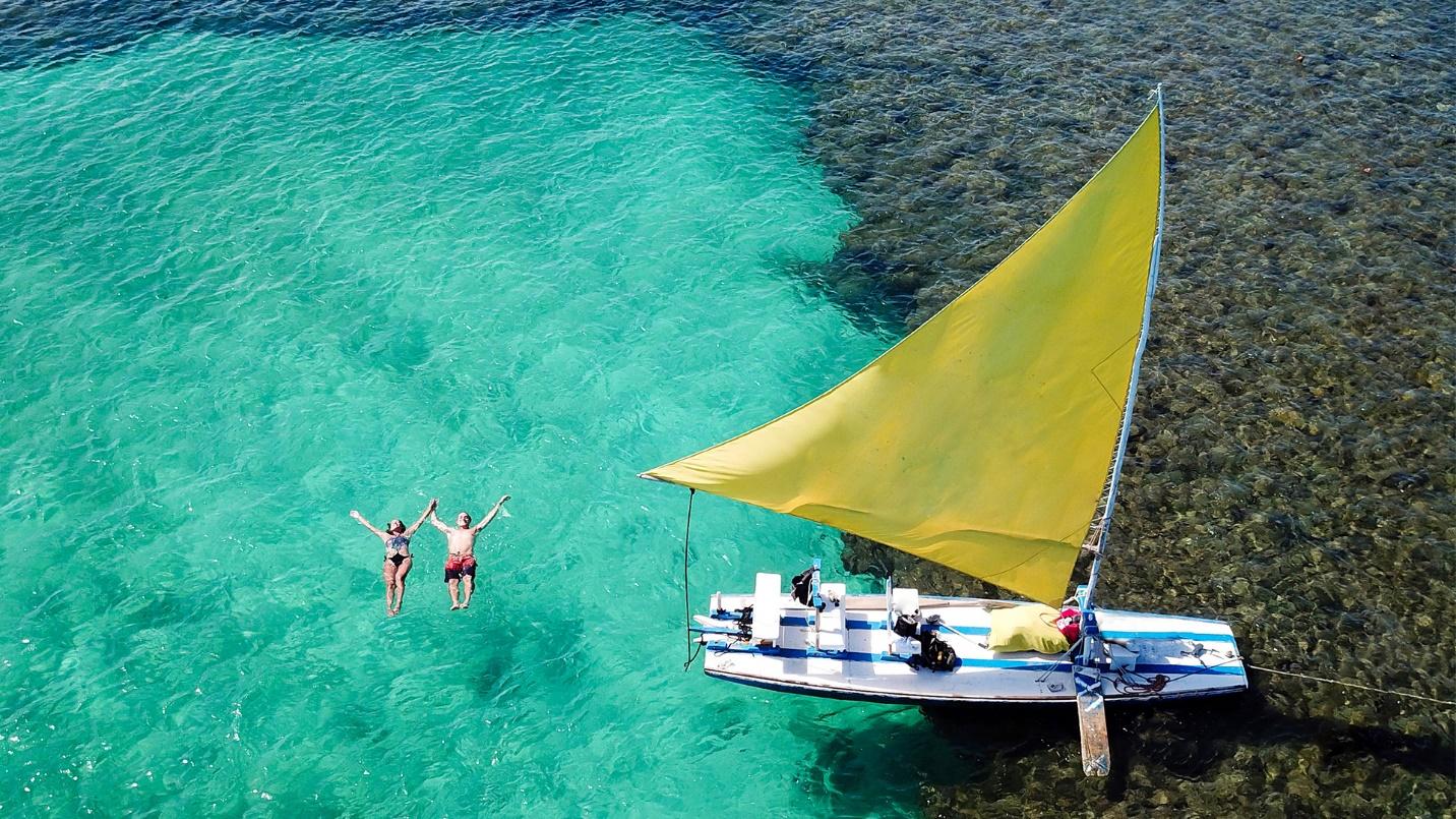 A couple with their arms outstretched float in a green sea beside their boat in a section about the neighborhood’s outdoor activities. 