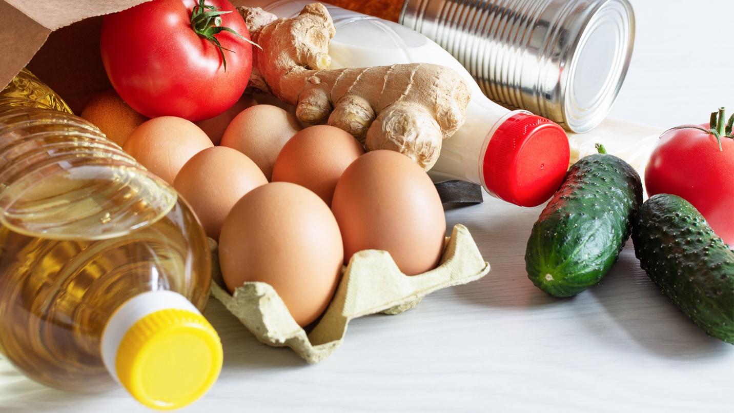 A paper bag with eggs, tomatoes, cucumbers, oil, milk, and cans in a section about groceries and their prices in San Juan.