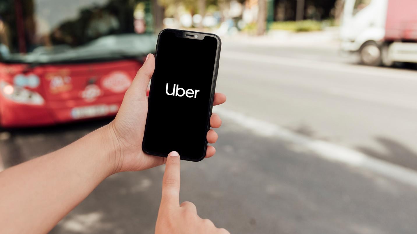 A person by the street holds a smartphone that displays “Uber” in a section about transportation and costs in Miramar.