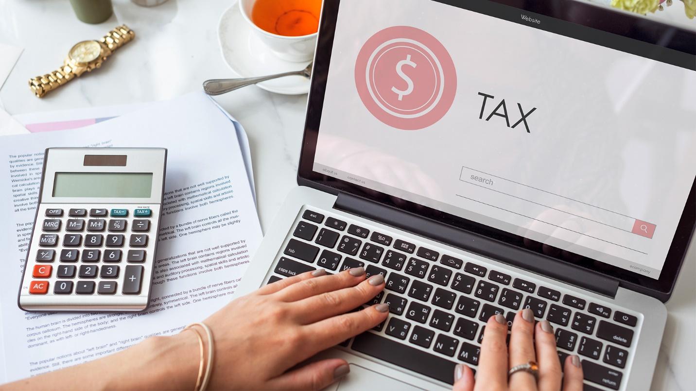 A woman sees the word “TAX” on a laptop at a table with a calculator, papers, and tea in a section about Act 60 tax benefits.