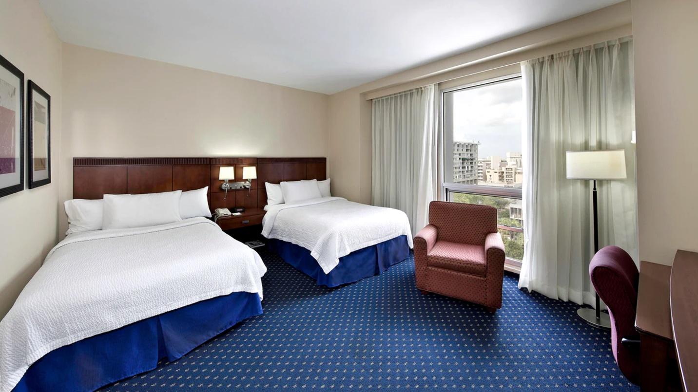 A room with two beds, a recliner, and blue carpet at Courtyard by Marriott San Juan Miramar in a section about area hotels. 