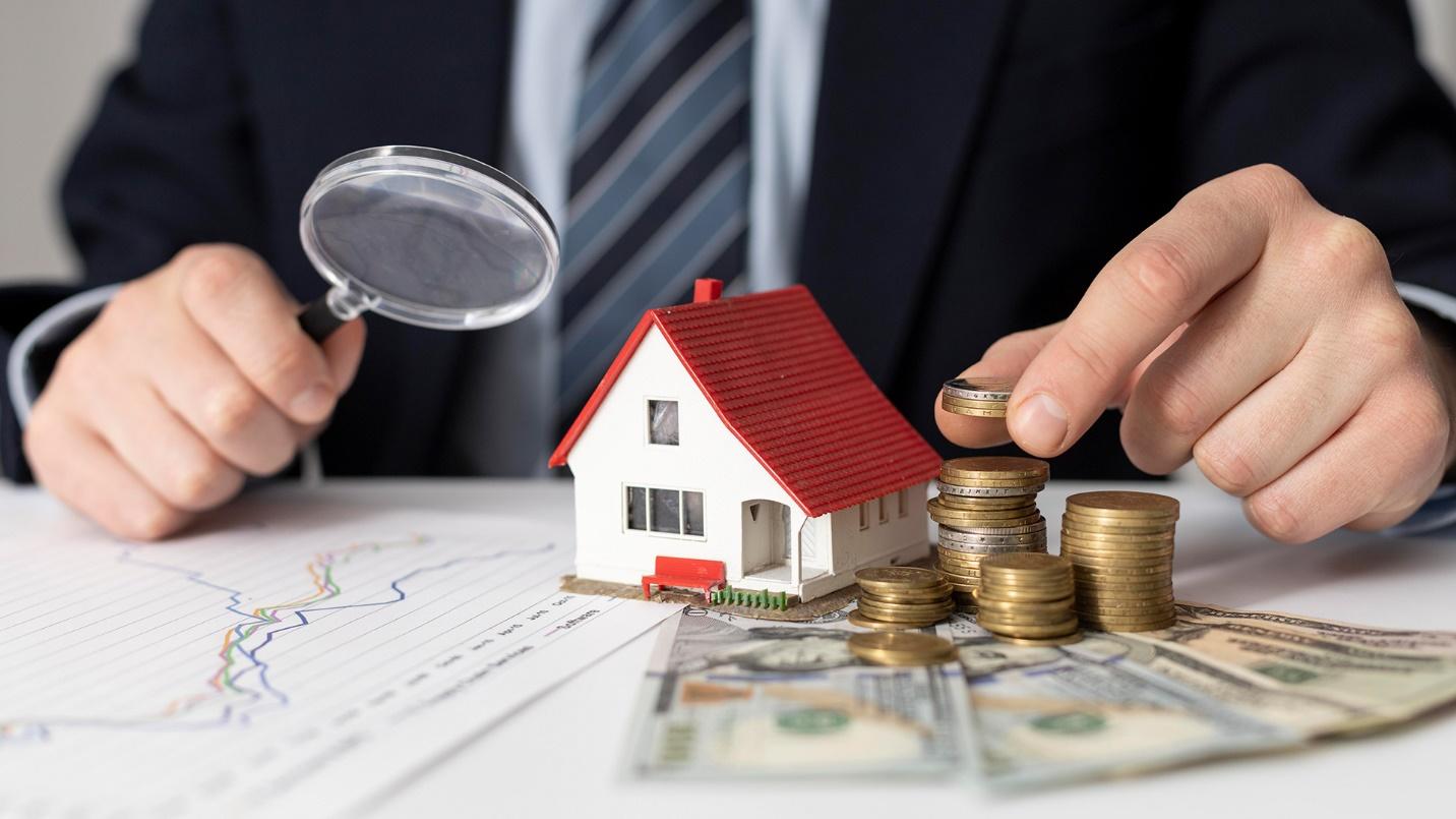 A man with a magnifying glass looks at money, a toy house, and charts in a section about Puerto Rico’s cost of living. 