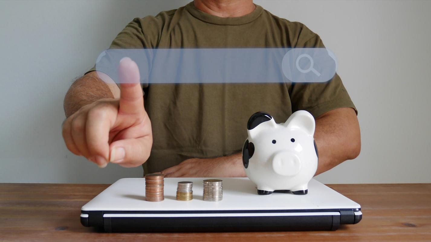 A person touching a screen with a laptop, some coins and a piggybank on them, symbolizing how to choose the right bank in puerto rico.