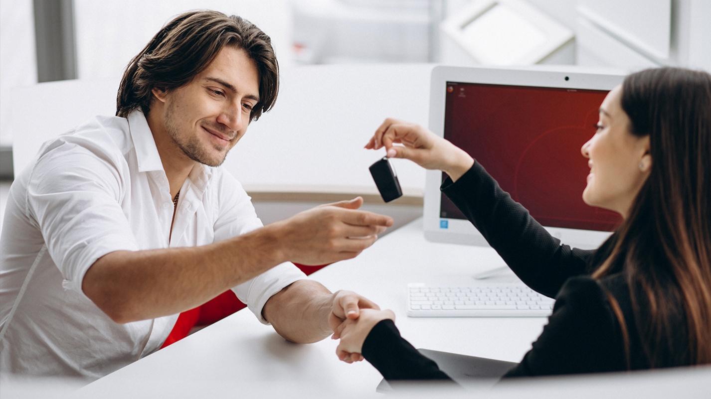 Smiling man receiving car keys from a rental agency representative at a modern office, symbolizing car rental services in Puerto Rico.