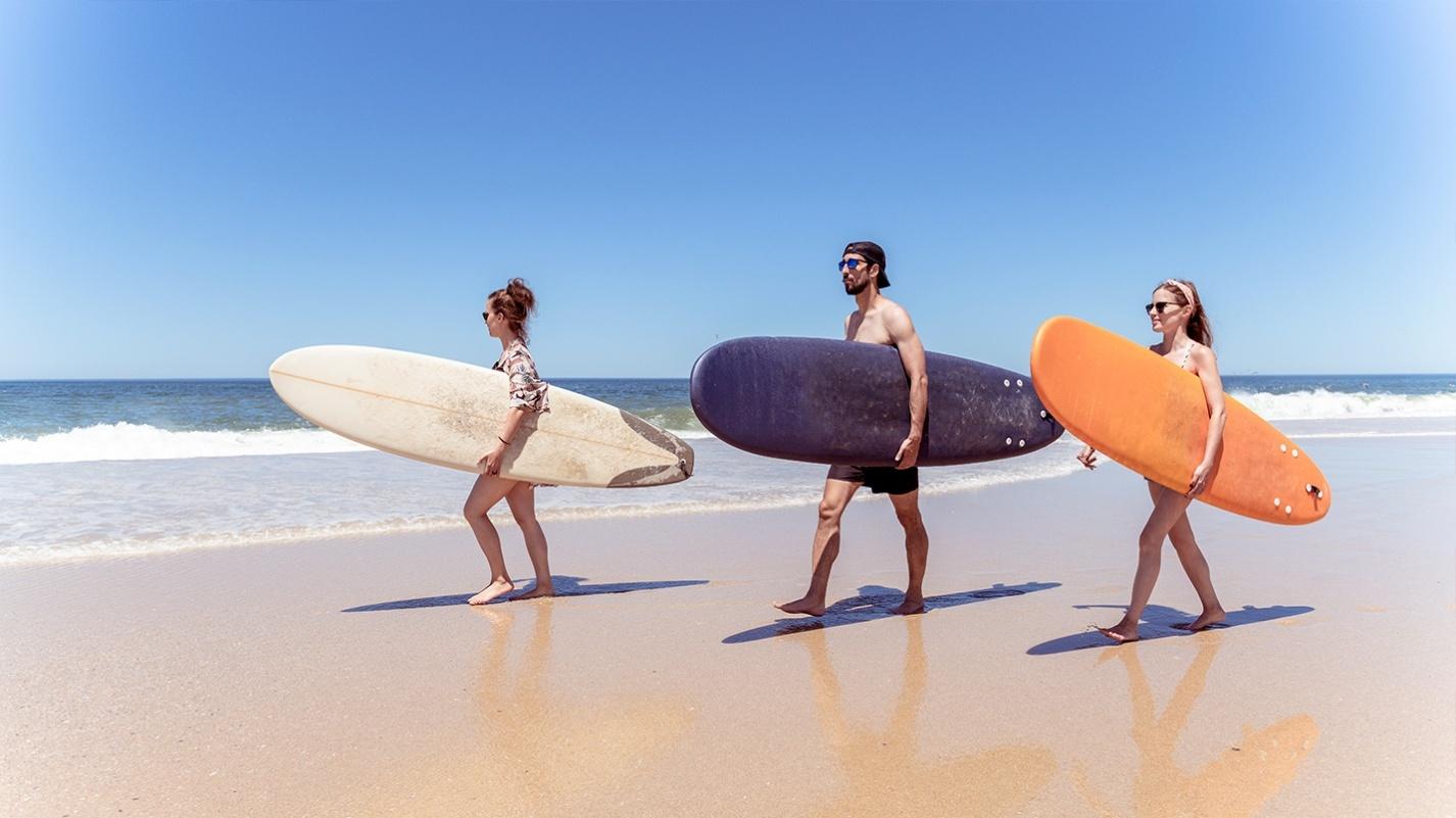 Three friends walking along a sunny Puerto Rico beach with surfboards, heading toward the waves—perfect for exploring the island’s top surfing spots like Rincón.