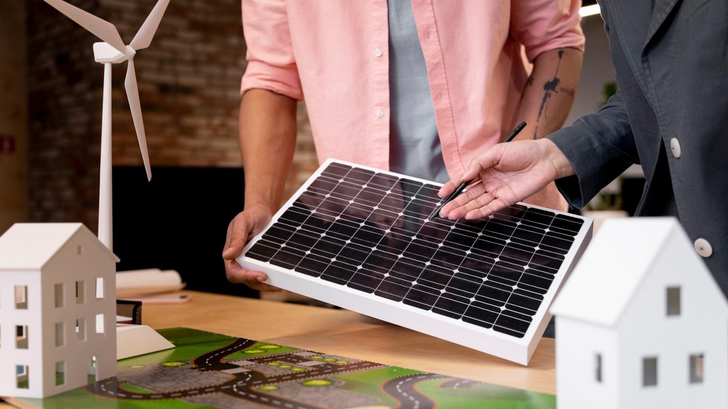 Two professionals reviewing a rooftop solar panel model alongside a miniature wind turbine and housing layout, symbolizing Puerto Rico’s shift to clean energy and infrastructure modernization.