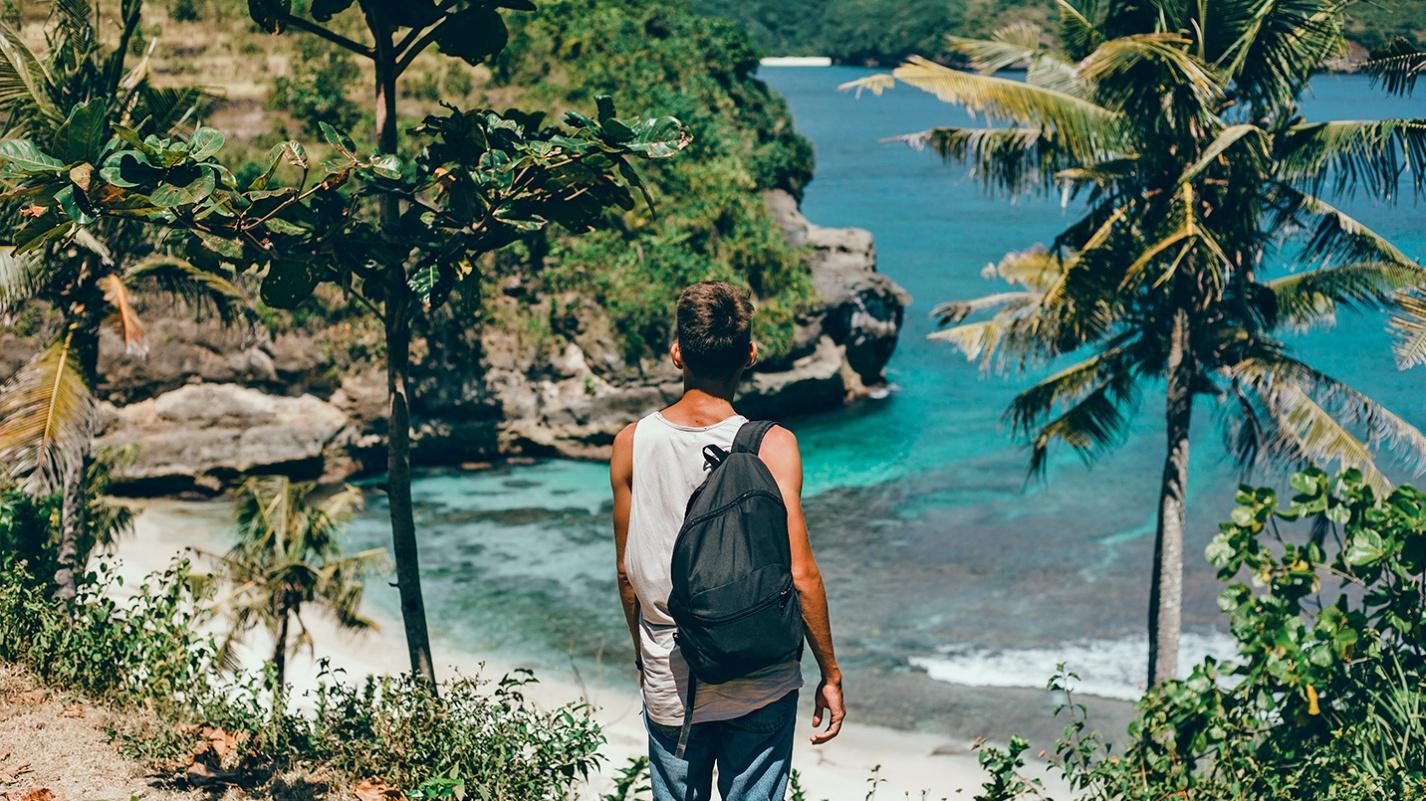 Traveler with a backpack overlooking a hidden cove surrounded by lush greenery in Puerto Rico, symbolizing beach exploration and natural beauty with the help of PRelocate.