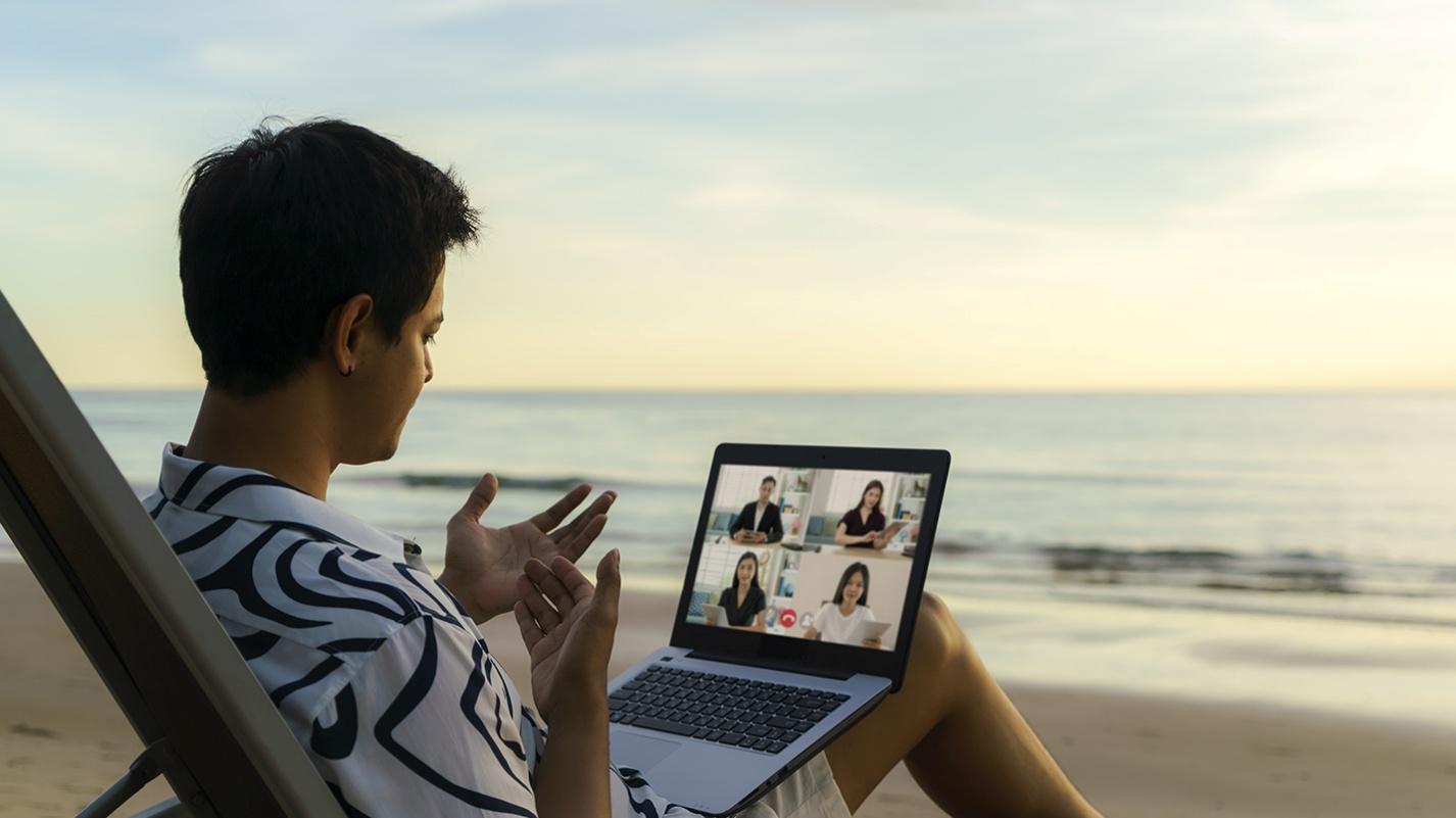 Remote worker in a tropical shirt joining a video call on a laptop while sitting by the beach in Puerto Rico, highlighting digital connectivity and lifestyle appeal for Act 60 residents.