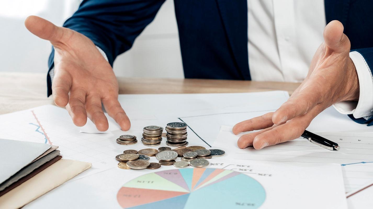 Businessman gesturing towards stacked coins on financial documents, representing strategic tax planning and financial management under Puerto Rico’s Act 60.