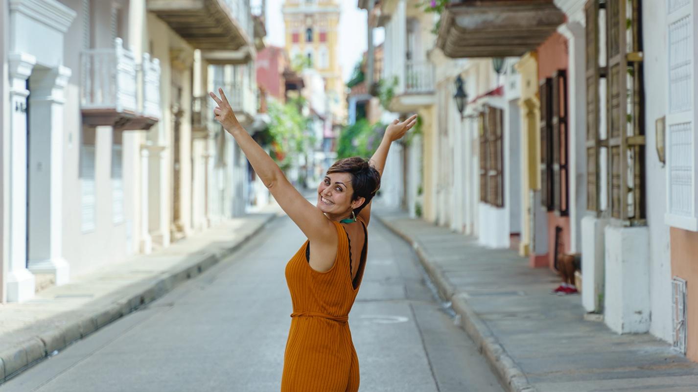 A smiling woman raises her arms joyfully on a colorful street, symbolizing the carefree lifestyle and warm community found in Puerto Rico neighborhoods.