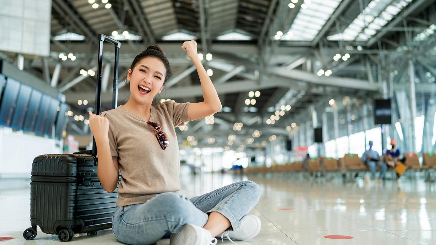 A happy traveler sitting on the floor of an airport next to her suitcase, celebrating the ease of domestic travel to Puerto Rico for U.S. citizens without needing a passport.