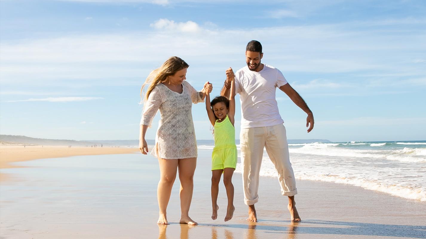 A smiling family with a young child walking along a sunny beach, highlighting Puerto Rico’s public beach access and relaxed, family-friendly coastal lifestyle.